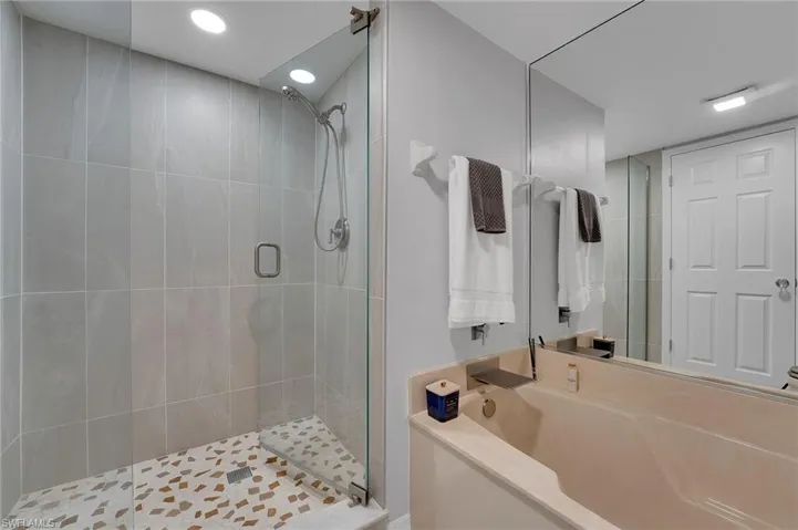 The primary suite bath is elevated with floor-to-ceiling porcelain tile and a seamless glass enclosure, creating a sleek, spa-like atmosphere defined by refined craftsmanship and modern luxury, complemented by a separate Zen-inspired soaking tub for ultimate relaxation.