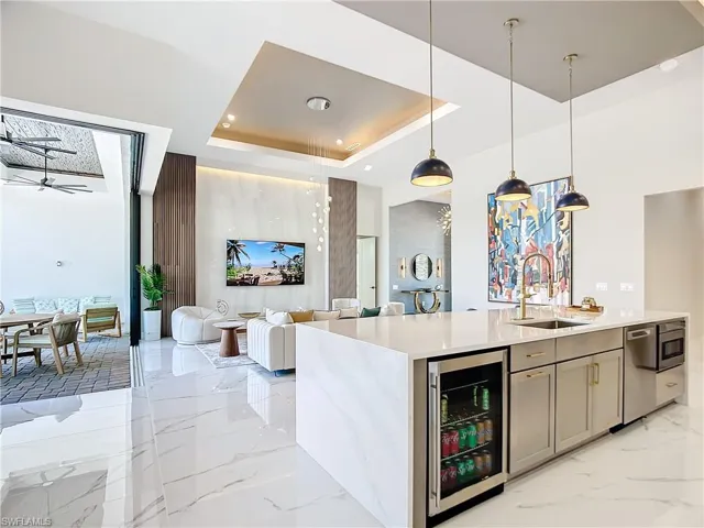 Kitchen with a raised ceiling, beverage cooler, ceiling fan, decorative light fixtures, and sink