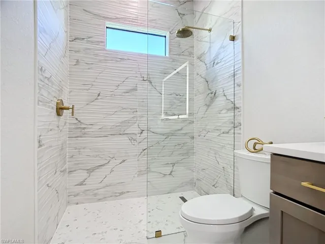 Bathroom featuring a tile shower, vanity, and toilet