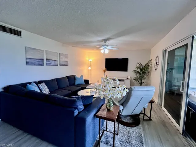 Great room area with TV and plank flooring stepping out to the enclosed lanai and views of the the golf course and water feature.