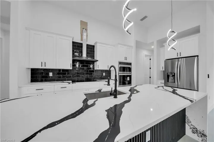 Kitchen with white cabinets, light stone countertops, stainless steel appliances, decorative backsplash, and hanging light fixtures