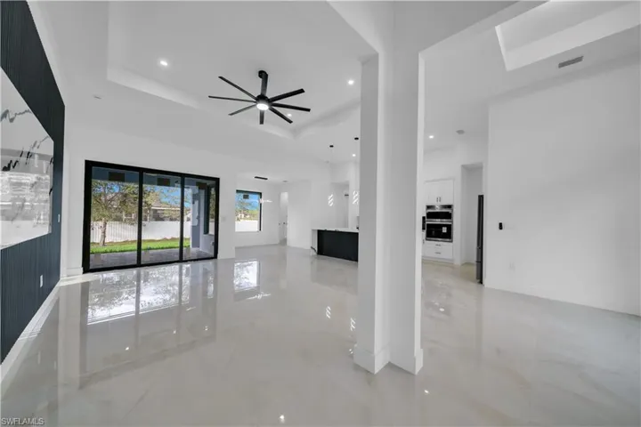 Unfurnished living room with a ceiling fan, light marble finish flooring, recessed lighting, and a tray ceiling