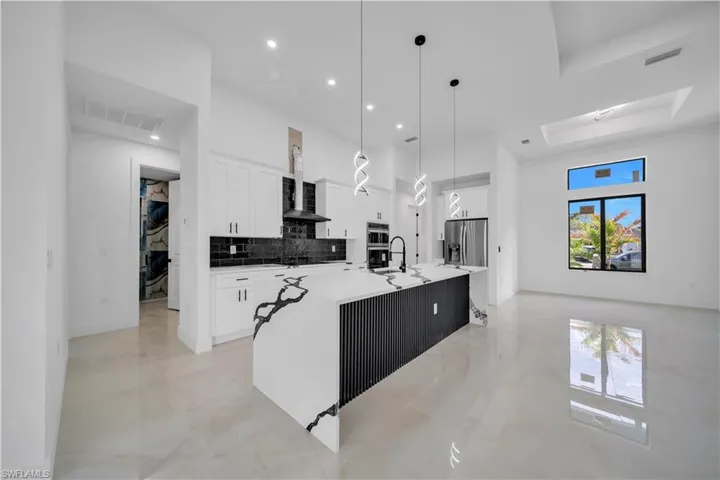 Kitchen with white cabinets, hanging light fixtures, light stone countertops, a spacious island, and light marble finish flooring