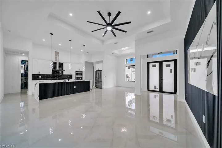 Two tone kitchen featuring open floor plan, a spacious island, ceiling fan, hanging light fixtures, and stainless steel appliances
