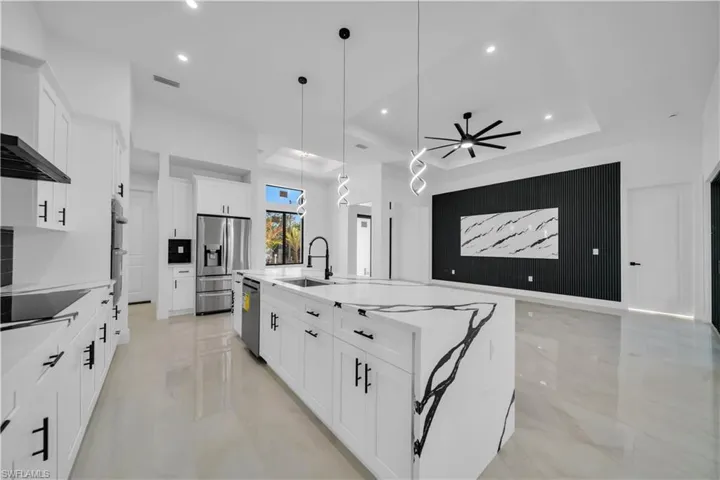 Kitchen featuring a spacious island, white cabinets, ceiling fan, light stone countertops, and stainless steel appliances