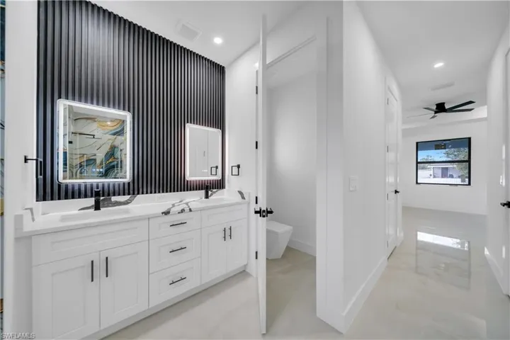 Full bathroom featuring double vanity, recessed lighting, an accent wall, and a ceiling fan