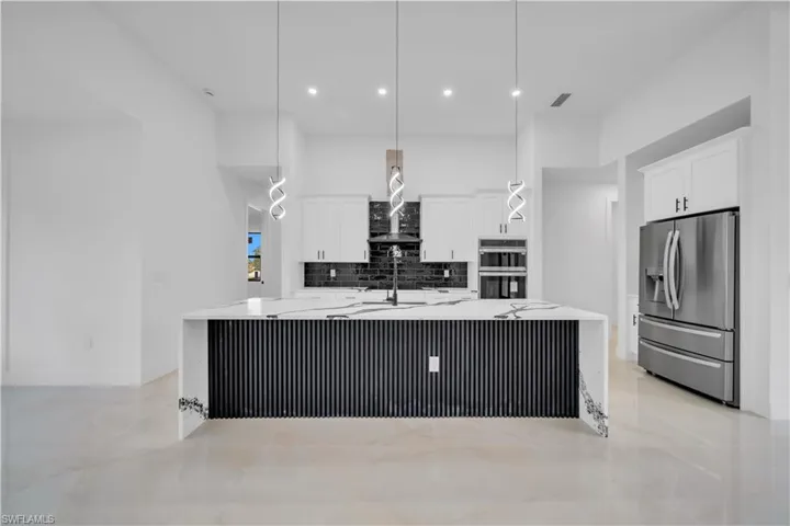 Kitchen with a large island, light stone countertops, decorative light fixtures, stainless steel appliances, and white cabinets