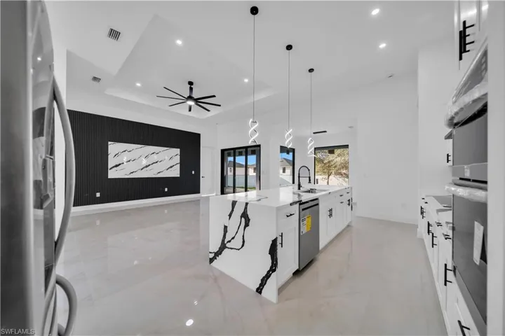 Kitchen featuring a spacious island, stainless steel appliances, light stone countertops, white cabinetry, and decorative light fixtures