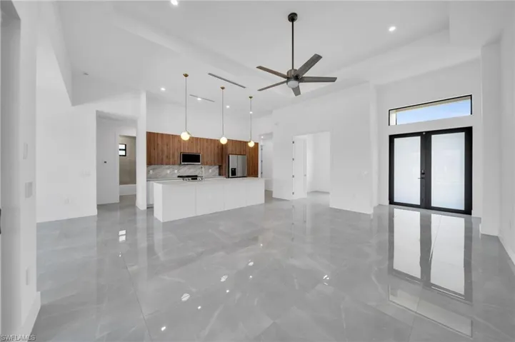 Unfurnished living room with a high ceiling, light marble finish flooring, recessed lighting, a ceiling fan, and french doors