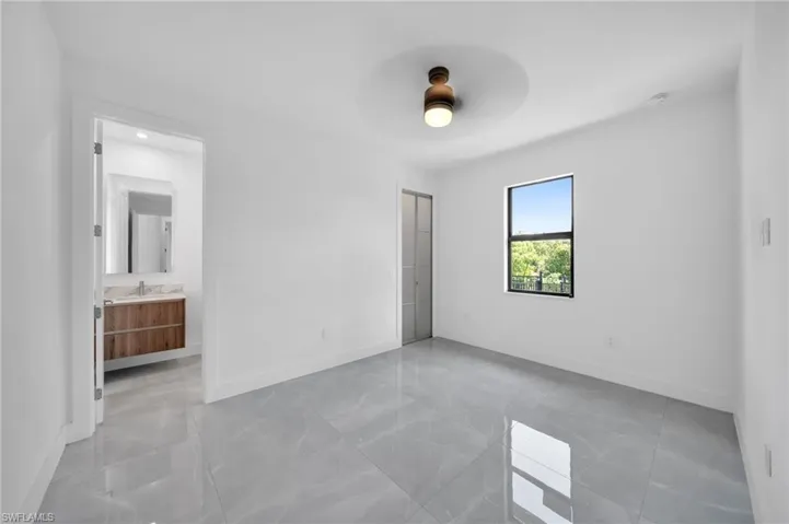 Unfurnished bedroom with ensuite bathroom, ceiling fan, and light marble finish floors