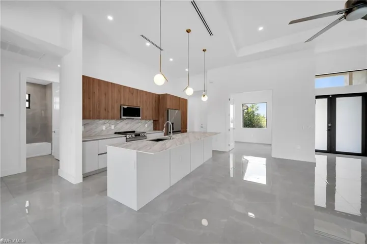 Kitchen with modern cabinets, brown cabinetry, a towering ceiling, pendant lighting, and an island with sink