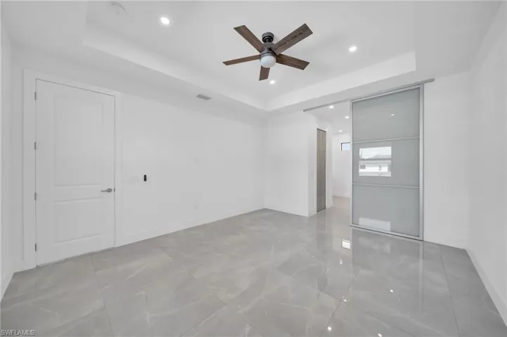 Empty room with a tray ceiling, recessed lighting, light marble finish floors, and ceiling fan