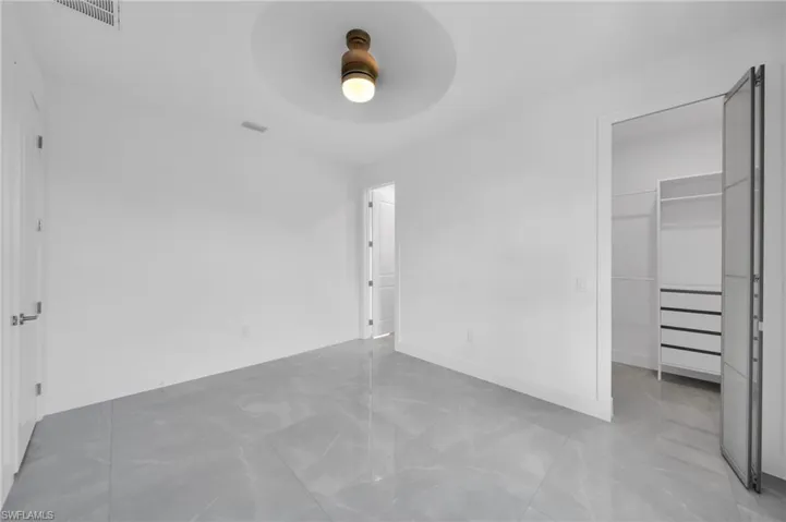 Unfurnished bedroom featuring a spacious closet, ceiling fan, and light marble finish floors