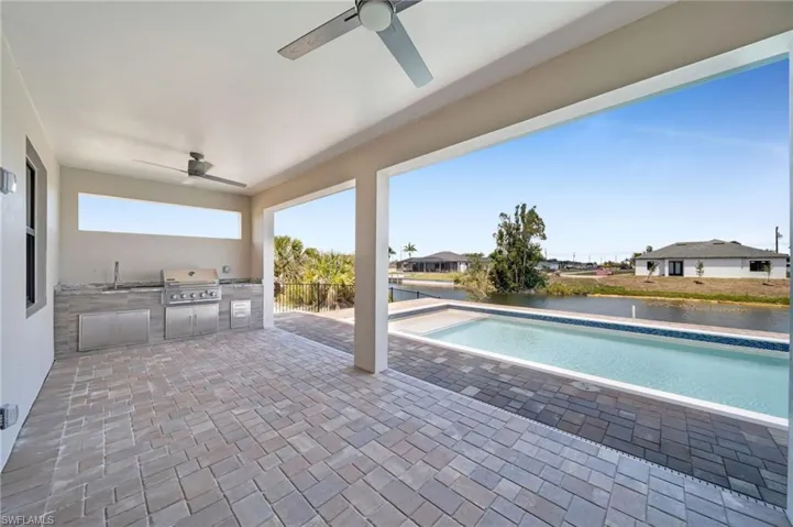 Swimming pool featuring exterior kitchen, a patio area, ceiling fan, and a water view