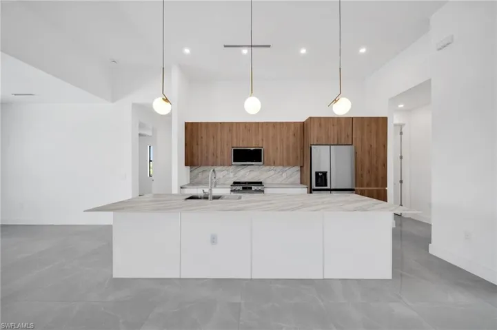 Kitchen featuring brown cabinets, decorative backsplash, appliances with stainless steel finishes, a large island, and pendant lighting