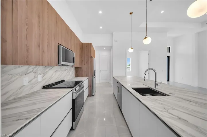 Kitchen with modern cabinets, appliances with stainless steel finishes, decorative light fixtures, light stone counters, and tasteful backsplash