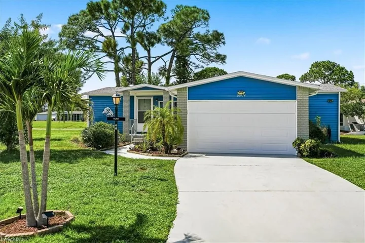 Blue exterior siding with light gray brick accents, white garage door, concrete driveway, and mature palm trees