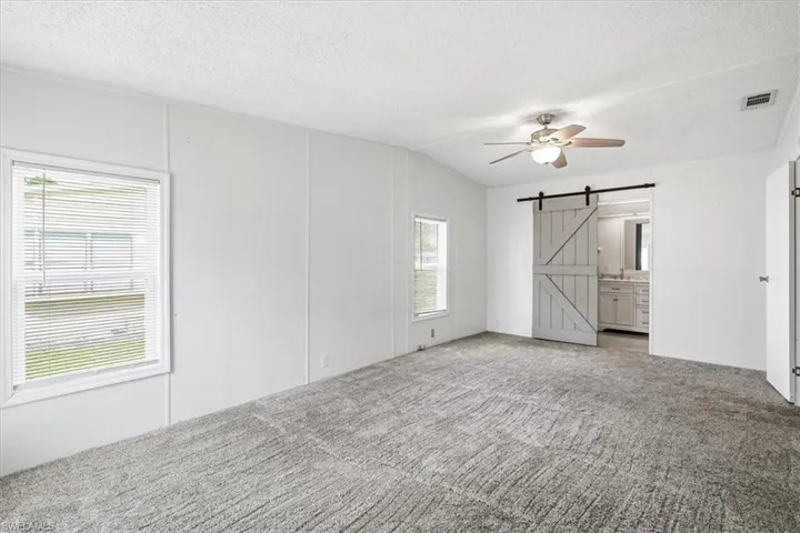 Spacious room with gray textured carpeting, white paneled walls, and a ceiling fan with integrated lighting