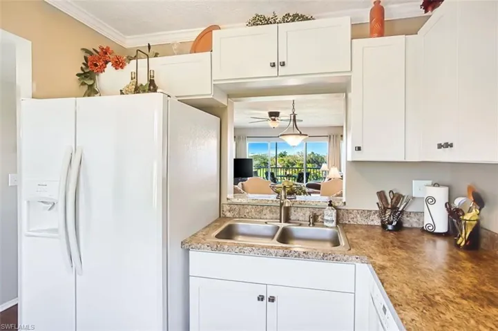 Kitchen featuring white refrigerator with ice dispenser, white cabinets, ornamental molding, ceiling fan, and pendant lighting