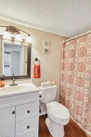 Full bath with vanity, dark wood-style floors, curtained shower, and a textured ceiling