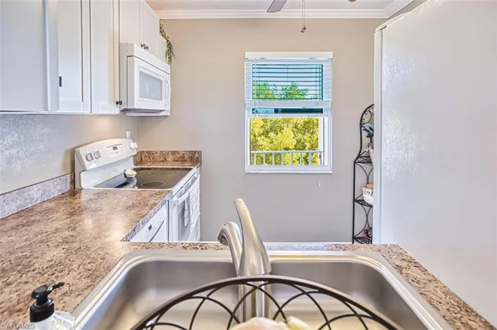 Kitchen featuring white appliances, white cabinets, ornamental molding, ceiling fan, and light countertops