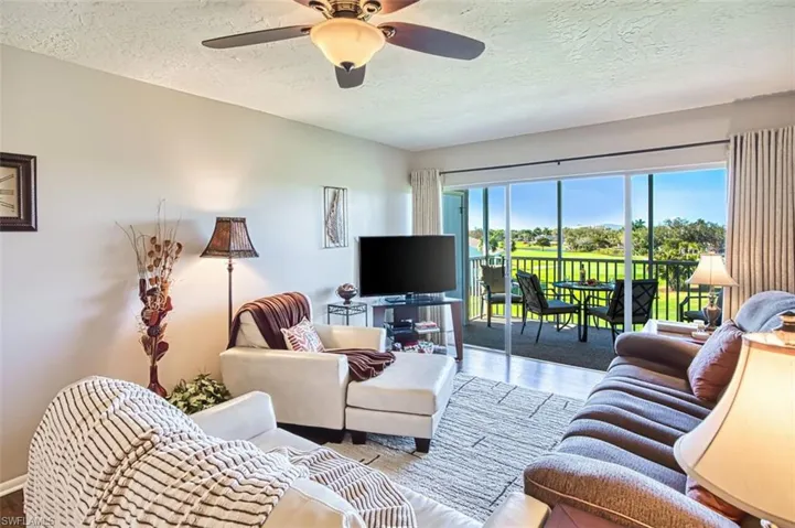 Living room with a textured ceiling, a ceiling fan, and wood finished floors