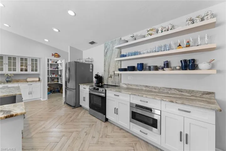 Kitchen featuring stainless steel appliances, light stone countertops, white cabinets, lofted ceiling, and light parquet flooring
