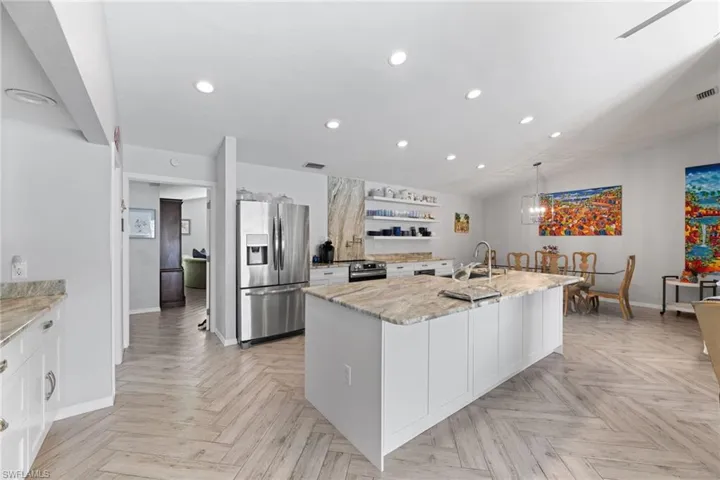 Kitchen featuring an island with sink, appliances with stainless steel finishes, white cabinetry, and light parquet floors