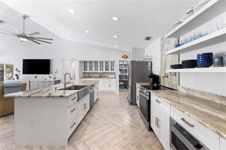 Kitchen featuring a center island with sink, sink, stainless steel appliances, white cabinets, and light parquet floors