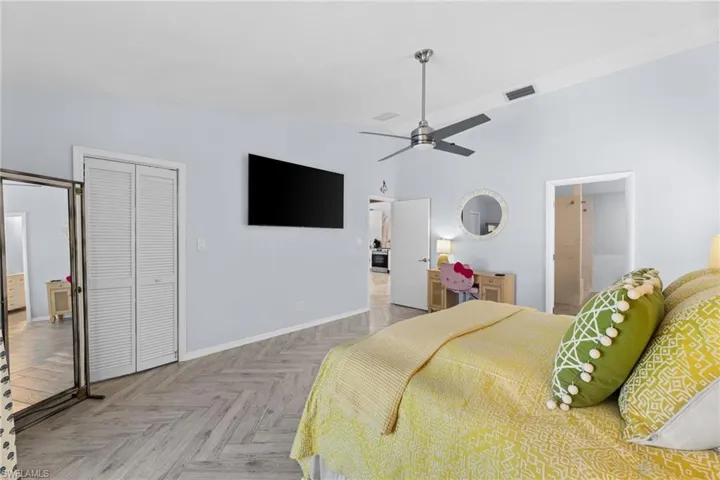 Bedroom with connected bathroom, a closet, light parquet flooring, ceiling fan, and high vaulted ceiling