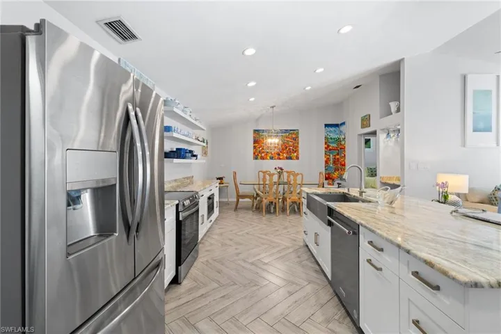 Kitchen featuring appliances with stainless steel finishes, light stone countertops, white cabinets, vaulted ceiling, and light parquet floors