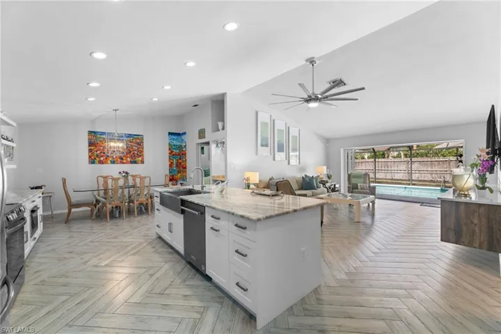 Kitchen with sink, light stone counters, vaulted ceiling, and white cabinets