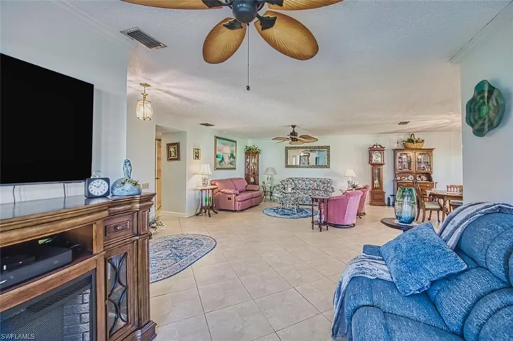 Living area featuring a textured ceiling, ornamental molding, light tile patterned flooring, and ceiling fan