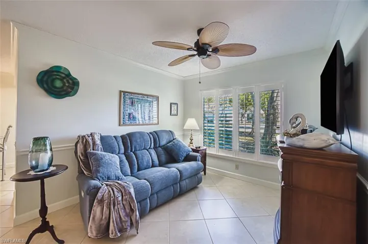 Living room featuring a textured ceiling, crown molding, light tile patterned floors, and ceiling fan