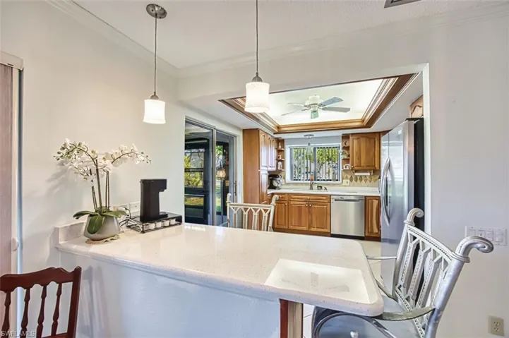 Kitchen featuring a tray ceiling, healthy amount of natural light, crown molding, hanging light fixtures, and brown cabinetry