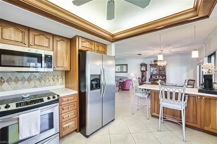 Kitchen featuring brown cabinets, stainless steel appliances, decorative light fixtures, crown molding, and tasteful backsplash