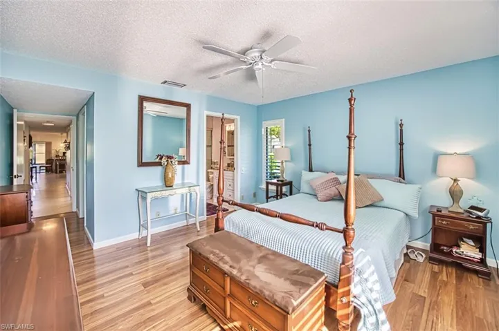 Bedroom with light wood-style floors, a textured ceiling, ensuite bath, and ceiling fan