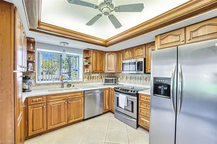Kitchen featuring appliances with stainless steel finishes, a tray ceiling, brown cabinets, ornamental molding, and light tile patterned floors