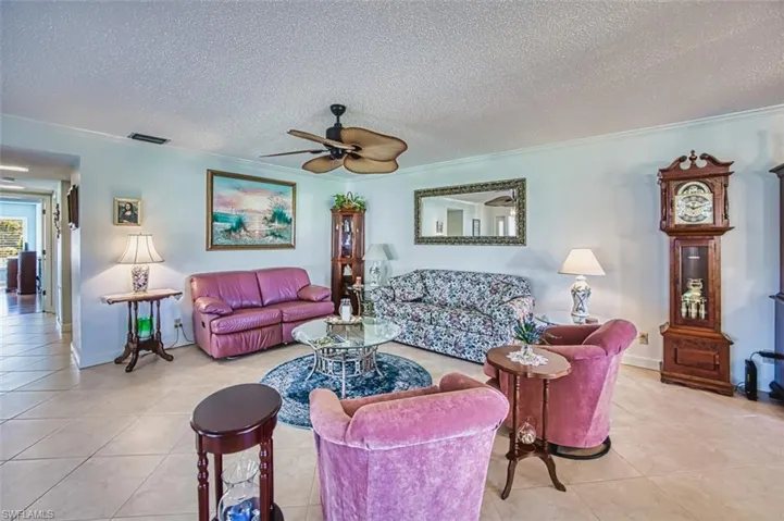 Tiled living room featuring a textured ceiling, a ceiling fan, and ornamental molding