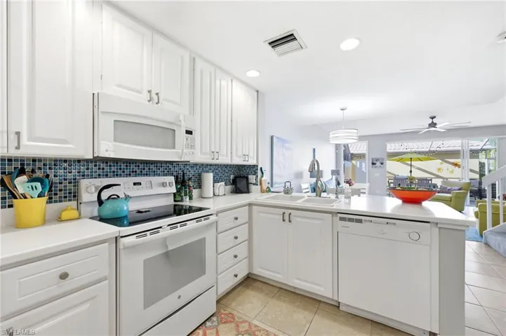 Kitchen with white appliances, white cabinetry, light countertops, a peninsula, and blue tile backsplash