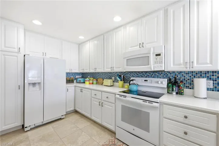 Kitchen featuring white appliances, white cabinets, light countertops,  blue tile backsplash, and recessed lighting