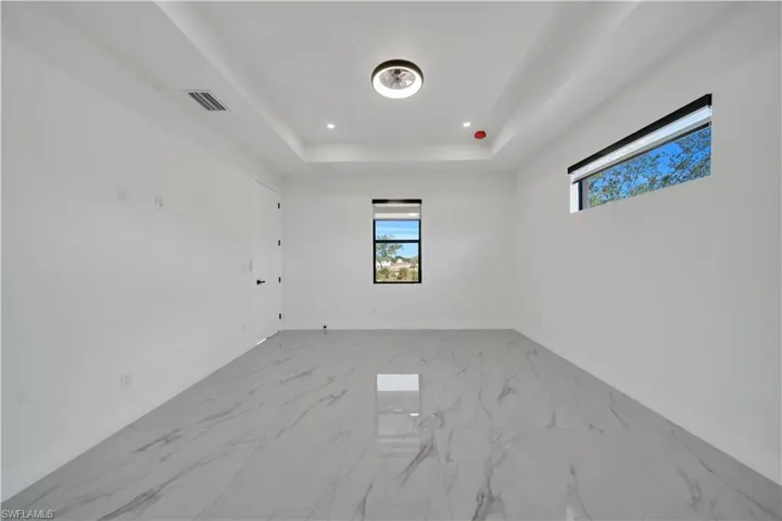 Empty room featuring a tray ceiling, light marble finish flooring, and recessed lighting