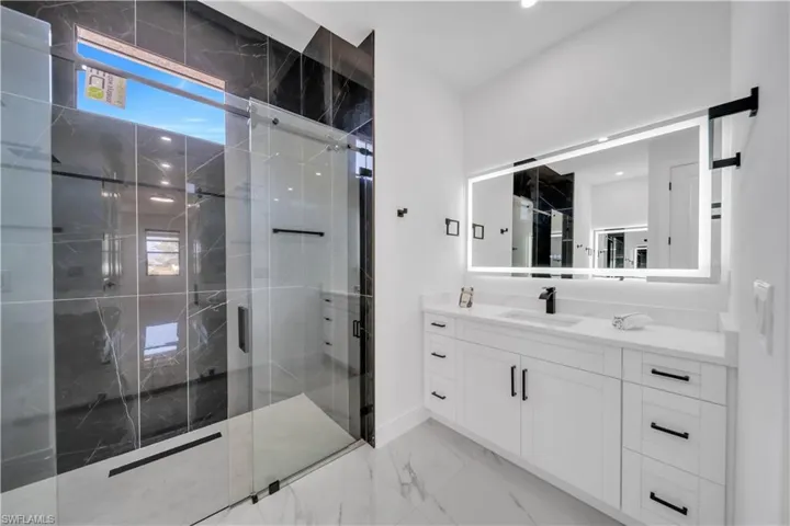 Full bath featuring vanity, a marble finish shower, light marble finish floors, and recessed lighting