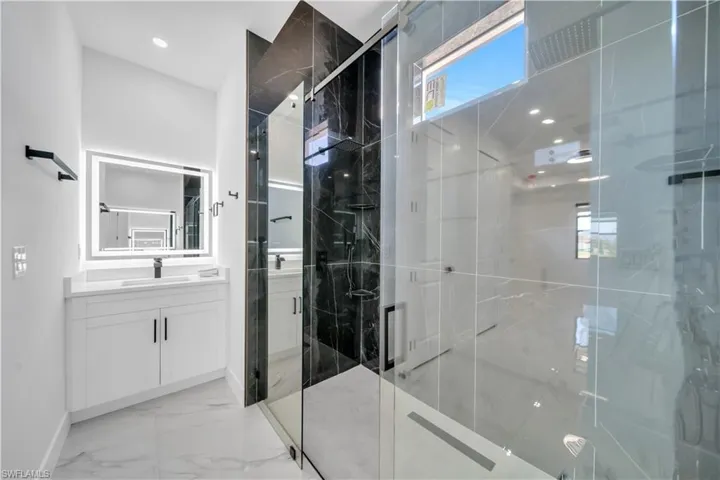 Bathroom featuring a marble finish shower, vanity, light marble finish flooring, and recessed lighting