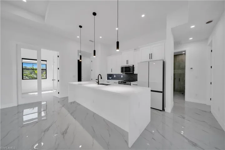 Kitchen with stainless steel appliances, white cabinetry, recessed lighting, hanging light fixtures, and light stone countertops