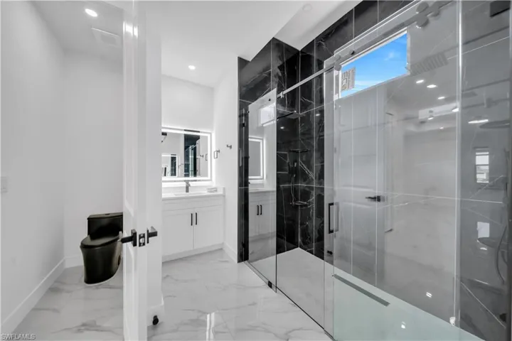 Bathroom with vanity, a marble finish shower, light marble finish floors, and recessed lighting