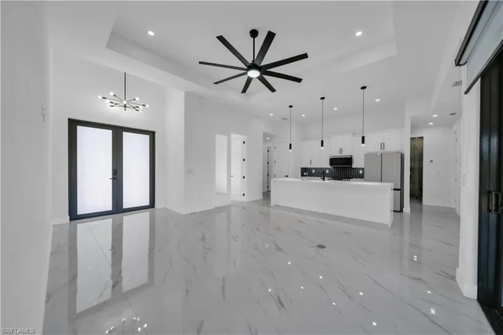 Unfurnished living room featuring a tray ceiling, a chandelier, light marble finish flooring, french doors, and recessed lighting