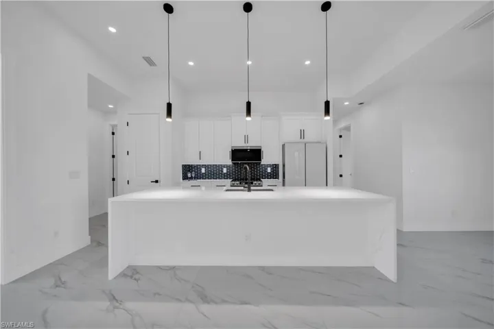 Kitchen with white cabinetry, tasteful backsplash, a large island, light stone countertops, and recessed lighting