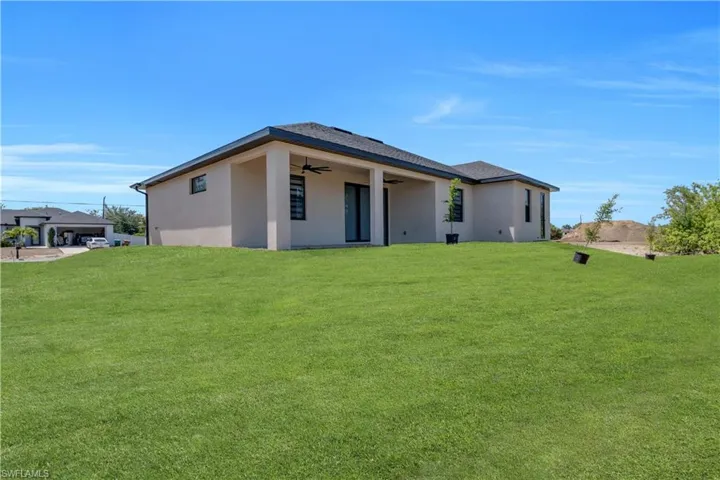 Rear view of property with ceiling fan, stucco siding, a yard, and a patio area