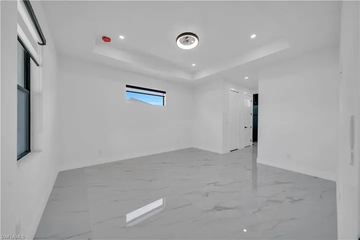 Unfurnished room featuring light marble finish flooring, a tray ceiling, and recessed lighting